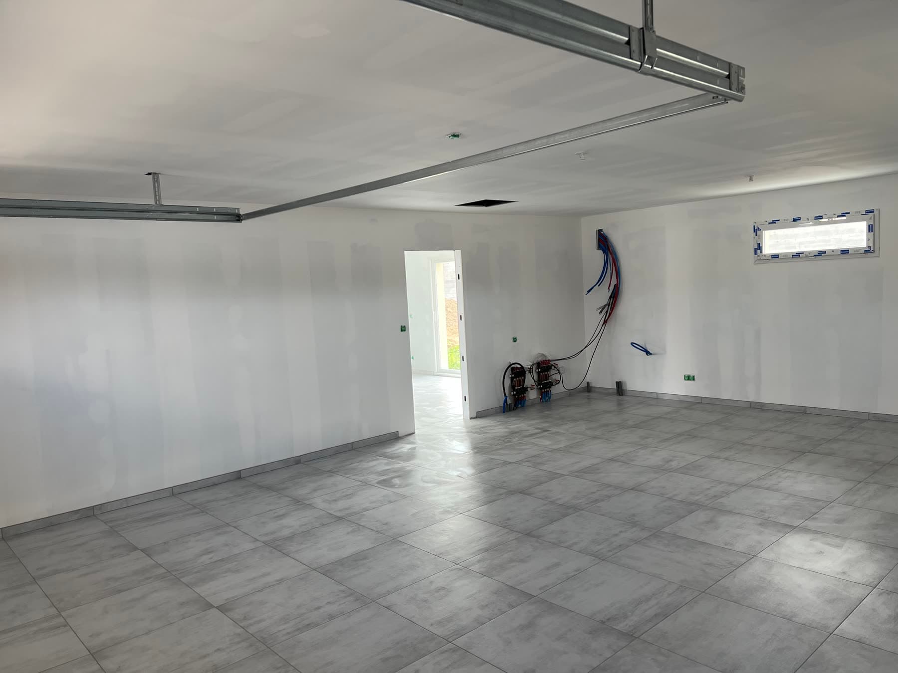 Garage carrelé avec porte sectionnelle et réseaux en attente.